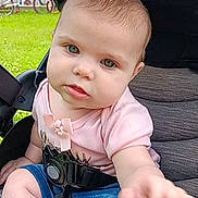 Nova joined the competition — help win amazing prizes! baby, child, stroller, outdoor, grass, bicycle, person, infant, summer, casual_clothing, pink_shirt, blue_shorts, seatbelt, greenery, daylight, curious, reaching_hand, background, building, play