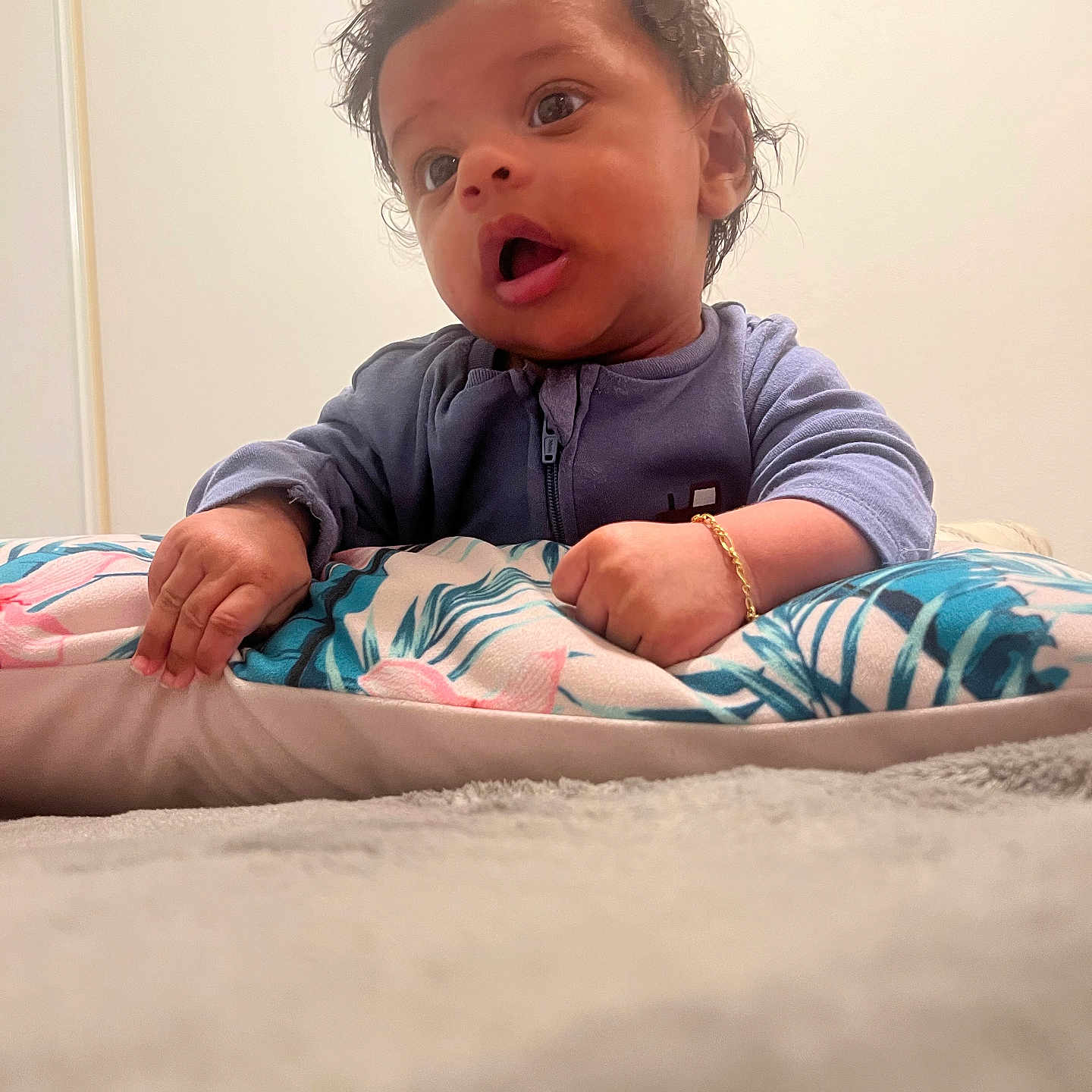 Allan participe au concours pour gagner de l'argent avec cette photo : baby, blanket, blue_clothing, bracelet, child, curly_hair, cute, expression, face, hand, home, indoor, infant, person, pillow, portrait, soft_texture, toddler, wall_art, wide_eyes