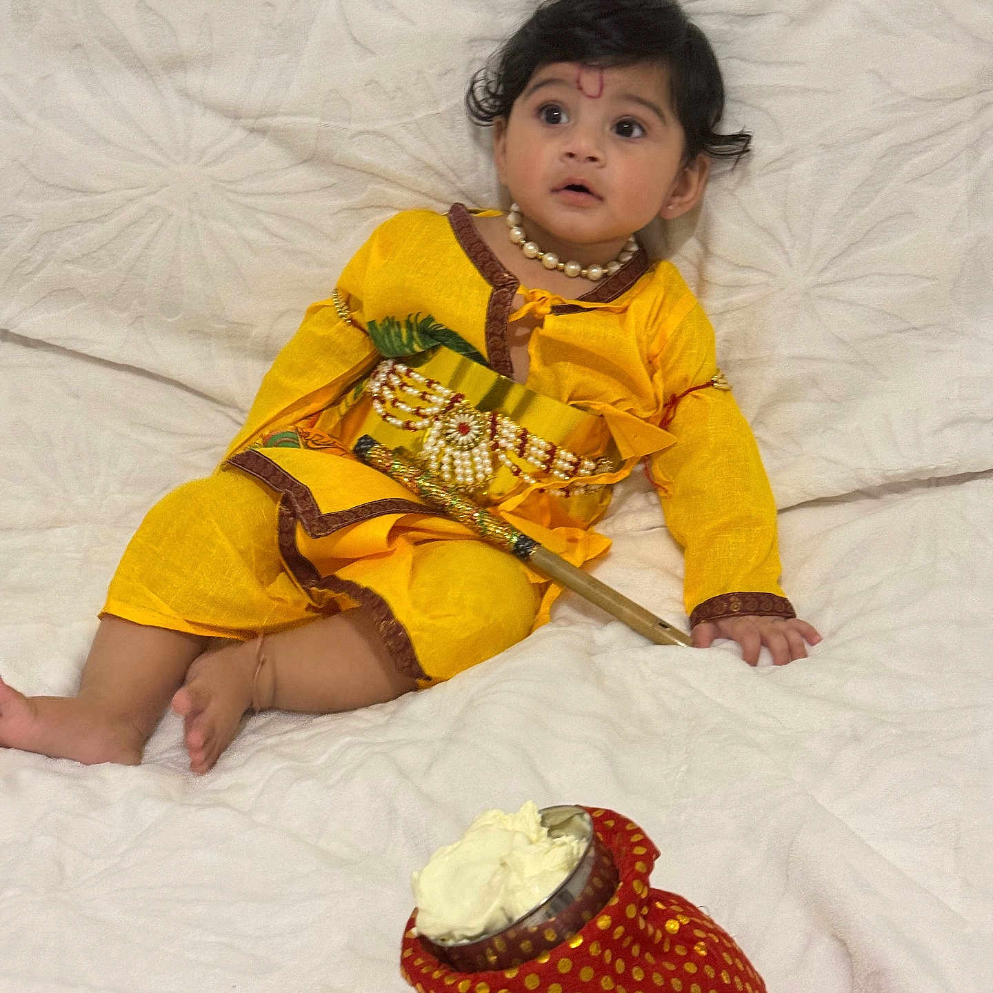 Devansh joined the competition — help win amazing prizes! baby, bracelet, child, cultural, curious, cute, decorative_stick, face, festive, footwearless, indoor, necklace, portrait, red_pouch, sitting, soft_texture, traditional_dress, white_blanket, yellow_clothing, young_child