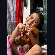 Andrea is registered to the contest to win money with this photo: child, smiling, teddy_bear, toy, blanket, clothing, indoors, portrait, happy, cute, person, face, hair, sitting, furniture, colorful, cozy, young, holding, expression