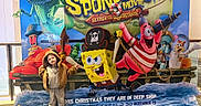 Andrea is registered to the contest to win money with this photo: child, cartoon, movie_poster, spongebob, pirate, costume, indoor, promotion, display, colorful, character, advertisement, smiling, clothing, footwear, carpet, playful, standing, young, beige