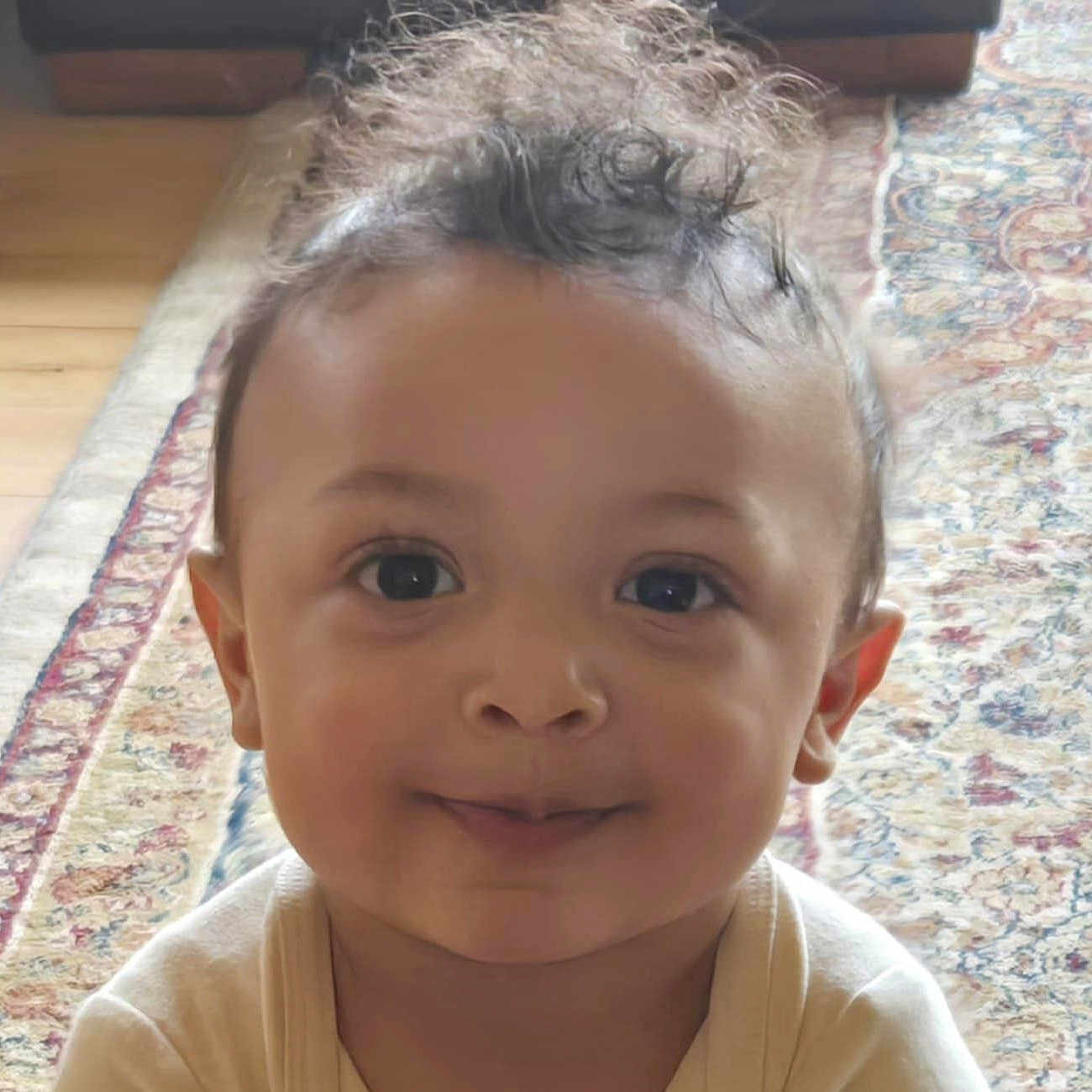 Blaise is registered to the contest to win money with this photo: baby, carpet, child, closeup, curly_hair, cute, eyes, face, happy, head, indoor, infant, light, natural_light, pattern, person, portrait, skin, smiling, young_child