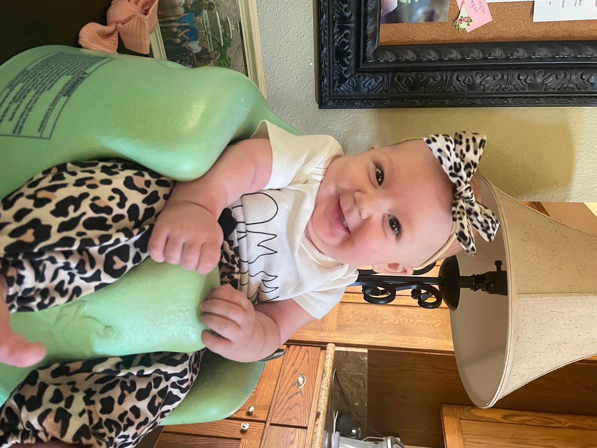 Macie is registered to the contest to win money with this photo: baby, baby_products, baby_toddler_clothing, child, comfort, fashion_accessory, happy, headgear, joy, linens, mammal, pattern, person, picture_frame, product, room, sitting, smile, toddler, wood