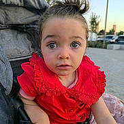 Giuliana participe au concours pour gagner de l'argent avec cette photo : toddler, child, stroller, red_dress, curious, outdoor, daylight, face, expression, hair_bun, clothing, hand, park, urban, person, seated, young, cute, baby, portrait