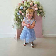 Amber is registered to the contest to win money with this photo: blue_dress, celebration, child, clapping, cute, decorations, floor, greenery, happy, holiday, indoor, pastel_colors, person, portrait, sandals, smiling, standing, toddler, wall, young_child