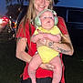 baby, car, child, clothing, evening, grass, happy, headphones, holding, nature, outdoor, person, portrait, red_shirt, road, smile, tattoo, trees, woman, yellow_onesie