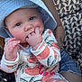 baby, child, hat, sun_hat, onesie, hand, fingers, person, nail_polish, tattoo, lap, patterned_fabric, geometric_pattern, outdoor, cute, infant, skin, face, blue_eyes, pink_nails