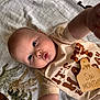 arm, baby, blanket, blue_eyes, child, cute, face, floor, half_birthday, hand, infant, lying_down, mouth, pattern, person, shirt, six_months, skin, text, wooden_tag