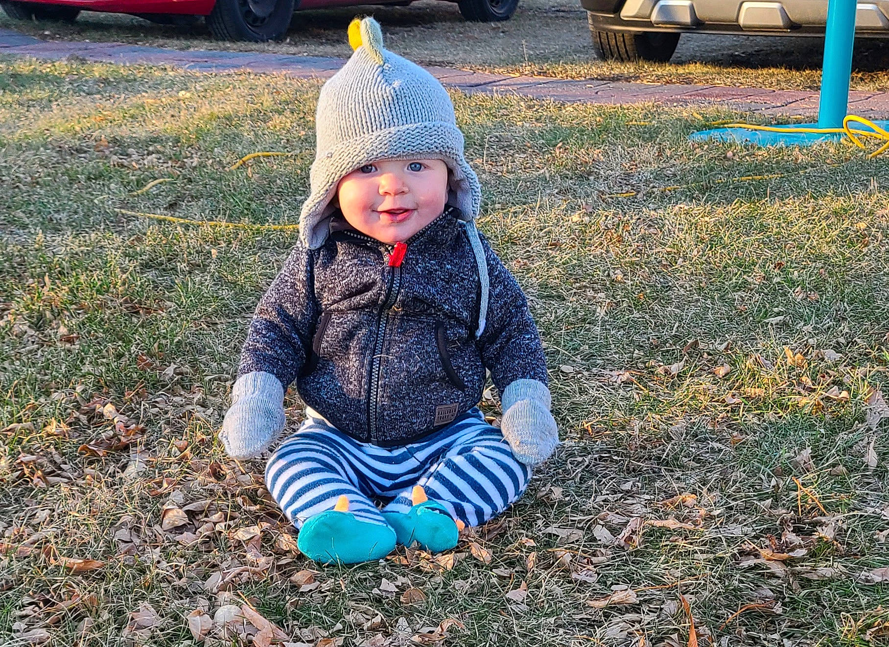 Keith is registered to the contest to win money with this photo: asphalt, automotive_tire, cap, fun, grass, happy, headwear, jacket, leaf, light, morning, people_in_nature, person, plant, public_space, road_surface, smile, tire, toddler, tree