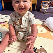 Mateo is registered to the contest to win money with this photo: baby, child, smiling, onesie, play_mat, floor, indoor, crib, mirror, reflection, hand, foot, happy, cute, infant, person, room, wooden_furniture, car_pattern, palm_tree_pattern