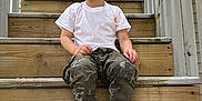 Carter joined the competition — help win amazing prizes! child, toddler, stairs, wood, smile, white_tshirt, camo_pants, black_sneakers, untied_laces, outdoor, railing, door, happy, casual, playful, young_child, portrait, sitting, daylight, wooden_steps