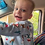 Carter is registered to the contest to win money with this photo: child, toddler, pajamas, car_interior, smiling, happy, person, window, seat, seatbelt, clothing, indoor, motion_blur, head, face, joy, holiday_theme, pattern, toy, family
