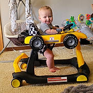 Oliver is registered to the contest to win money with this photo: baby, baby_swing, blanket, carpet, child, child_playing, foot, happy, indoor, person, playroom, racing_car, room, seat, smiling, toddler, toy, toy_animal, walker, yellow