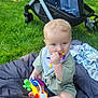 Oliver is registered to the contest to win money with this photo: baby, blanket, blue_eyes, chewing, child, clothing, colorful, cute, fun, grass, infant, nature, outdoor, park, playing, relaxing, sitting, stroller, teething_ring, toys