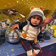 Sultan is registered to the contest to win money with this photo: toddler, child, hat, animal_hat, disco_balls, reflection, yellow_background, red_carpet, striped_socks, sitting, hand, indoor, playful, curious, cute, knitwear, casual_clothing, toy, decor, person
