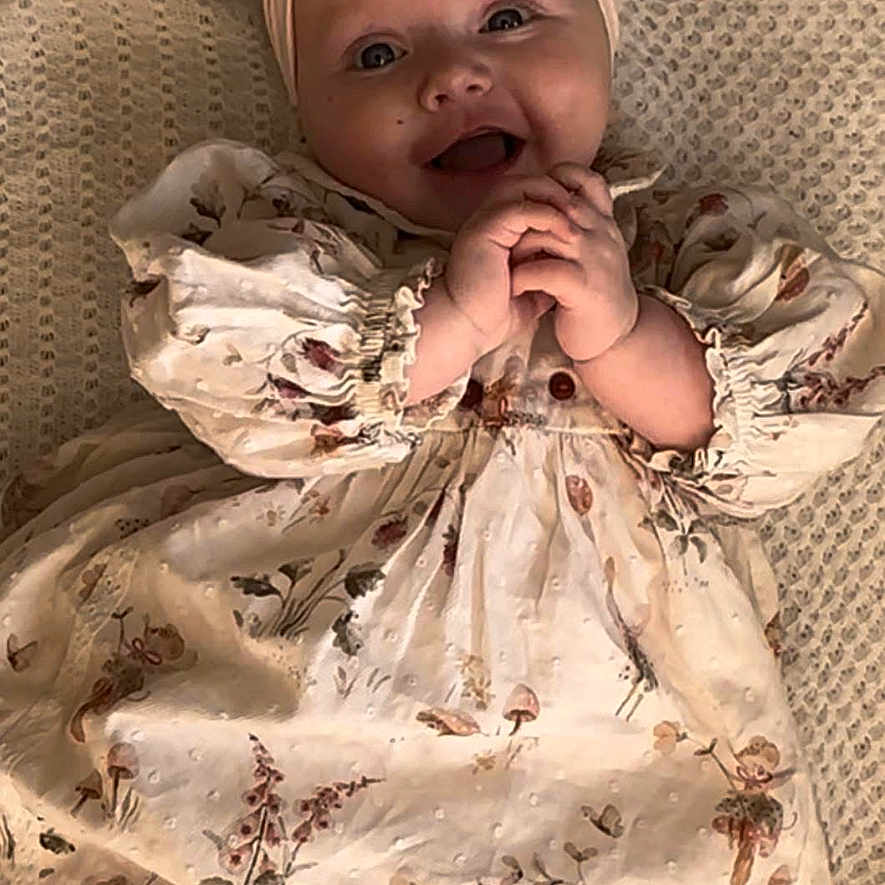 Mhiran joined the competition — help win amazing prizes! baby, bow, child, clothing, cute, face, floral_dress, hands, happy, headband, indoors, infant, knitted_blanket, lying_down, person, pink_tights, portrait, smiling, soft_lighting, toddler