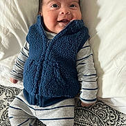 Christopher joined the competition — help win amazing prizes! baby, smiling, infant, blue_vest, striped_clothing, lying_down, bed, pillow, patterned_bedspread, happy, cute, child, young, cozy, portrait, indoor, apparel, person, face, head