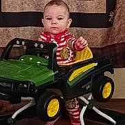 Levi joined the competition — help win amazing prizes! baby, child, walker, toy_car, john_deere, pajamas, indoors, floor, feet, face, person, furniture, home, decor, childrens_toy, footwear, expressionless, standing, room, playtime