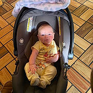 Matthew is registered to the contest to win money with this photo: baby, car_seat, blanket, flooring, wooden_floor, pajamas, child, indoor, seat, infant, clothing, footwear, person, smiling, cute, comfortable, toddler, baby_carrier, pattern, soft