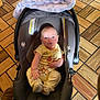 baby, car_seat, blanket, flooring, wooden_floor, pajamas, child, indoor, seat, infant, clothing, footwear, person, smiling, cute, comfortable, toddler, baby_carrier, pattern, soft