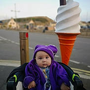 Stella-May joined the competition — help win amazing prizes! baby, child, purple_blanket, purple_hat, stroller, ice_cream_sculpture, outdoor, street, road, sidewalk, blurred_background, daytime, curious_expression, winter_clothing, urban, child_portrait, infant, cozy, wide_eyes, soft_lighting
