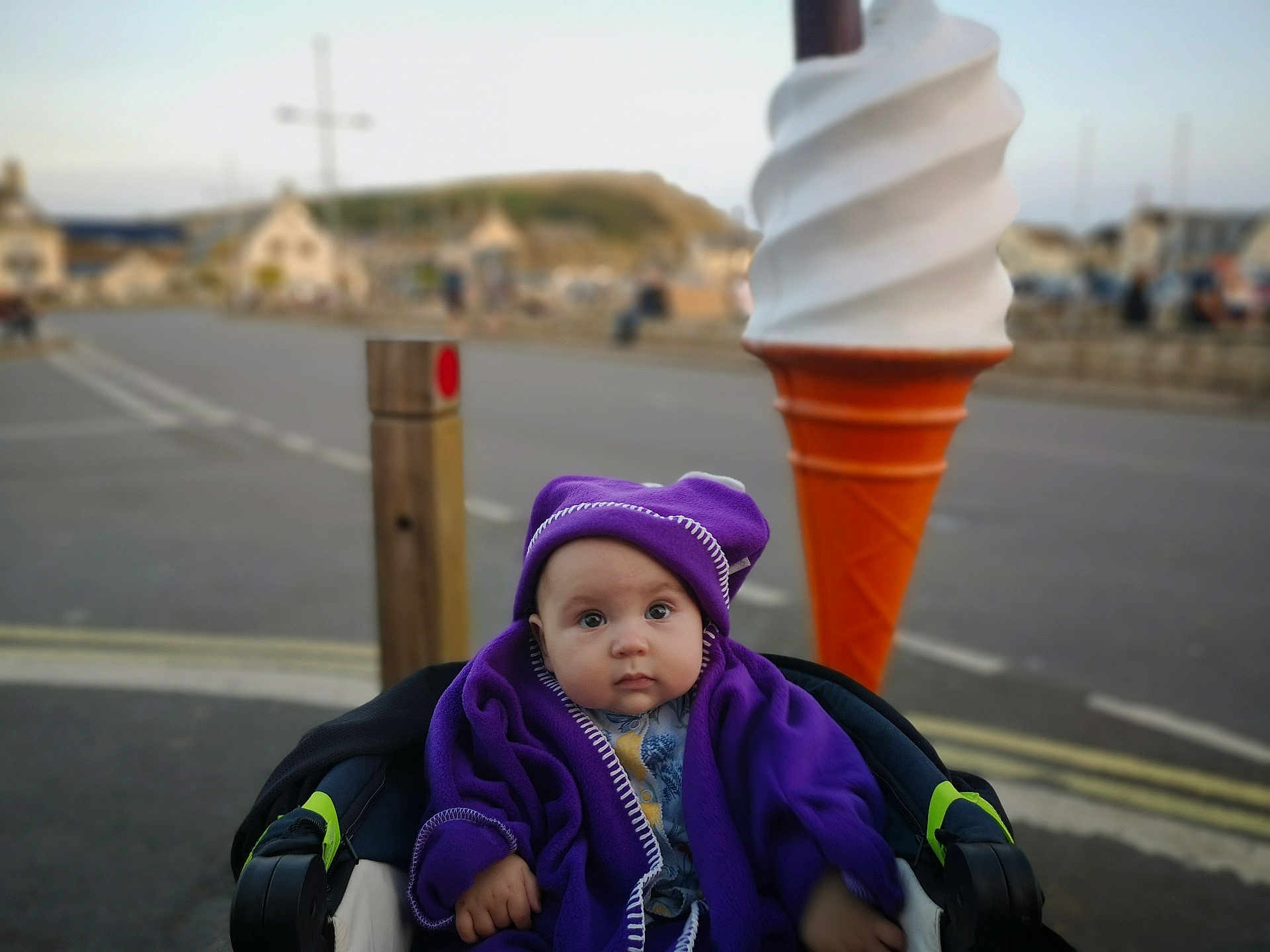 Stella-May joined the competition — help win amazing prizes! baby, child, purple_blanket, purple_hat, stroller, ice_cream_sculpture, outdoor, street, road, sidewalk, blurred_background, daytime, curious_expression, winter_clothing, urban, child_portrait, infant, cozy, wide_eyes, soft_lighting