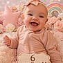 baby, infant, smiling, portrait, headband, bow, pink, pastel_background, flowers, plush_blanket, star_pillow, rainbow, milestone_sign, wooden_sign, sitting, cozy, cute, blanket, rosy_cheeks, studio_photo