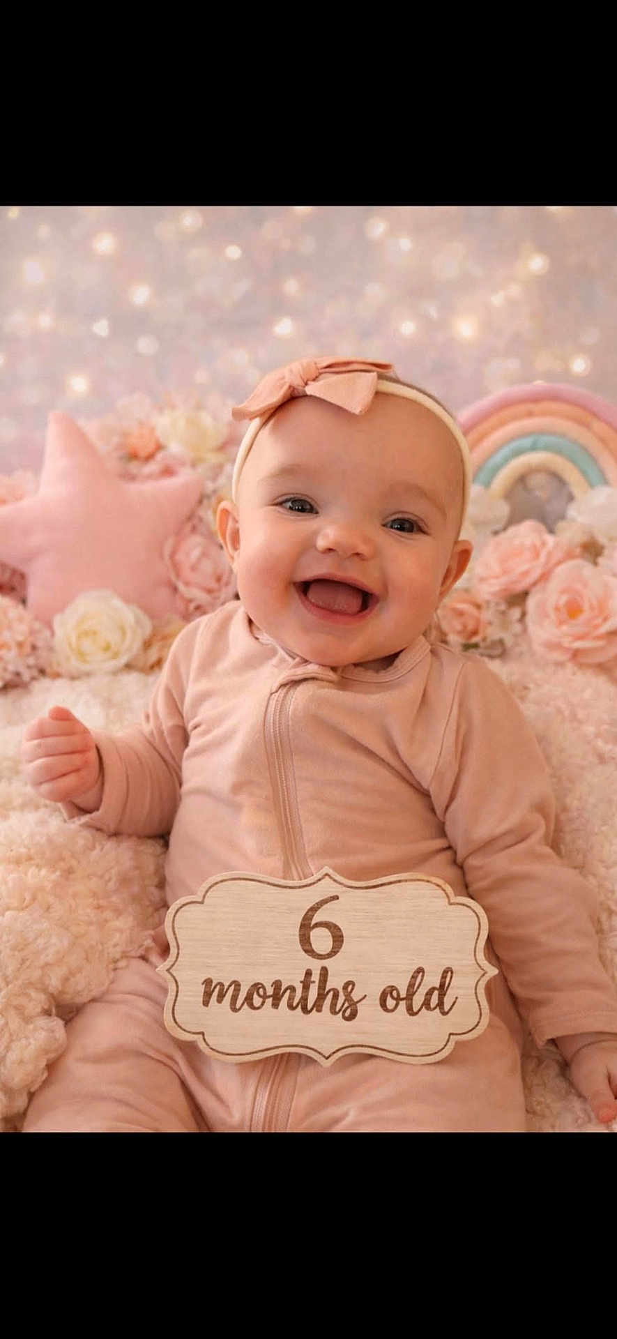 Ellie is registered to the contest to win money with this photo: baby, infant, smiling, portrait, headband, bow, pink, pastel_background, flowers, plush_blanket, star_pillow, rainbow, milestone_sign, wooden_sign, sitting, cozy, cute, blanket, rosy_cheeks, studio_photo