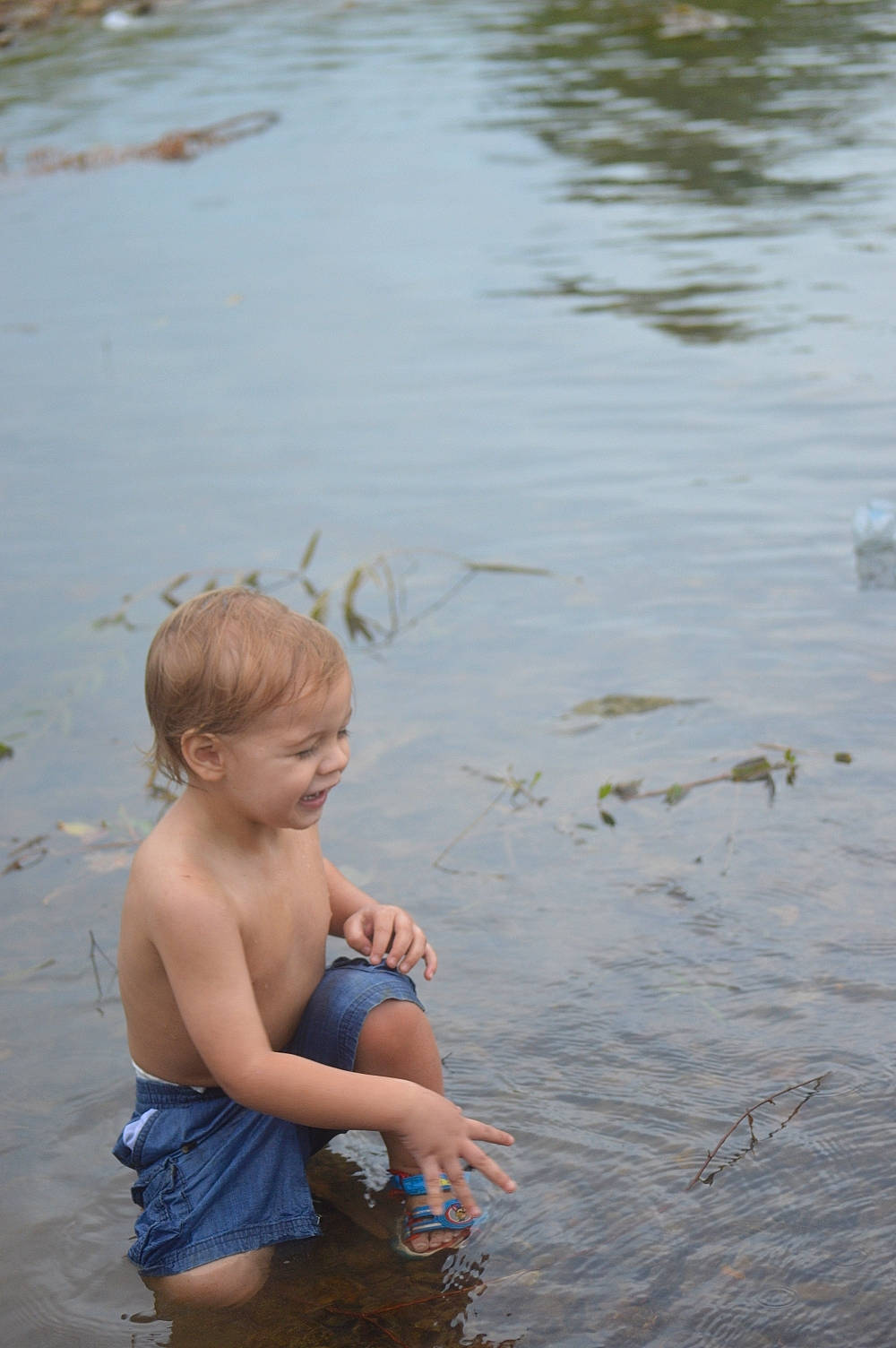 Damian is registered to the contest to win money with this photo: arm, barechested, barefoot, bathing, body_of_water, eye, fun, gesture, grass, hand, happy, human_body, lake, leisure, people_in_nature, people_on_beach, person, shorts, toddler, vertebrate