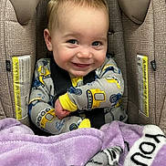 Paxton joined the competition — help win amazing prizes! baby, child, car_seat, blanket, smile, happy, infant, face, clothing, seatbelt, yellow, purple, cute, portrait, sitting, indoors, young, person, safety, cozy