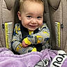 baby, child, car_seat, blanket, smile, happy, infant, face, clothing, seatbelt, yellow, purple, cute, portrait, sitting, indoors, young, person, safety, cozy