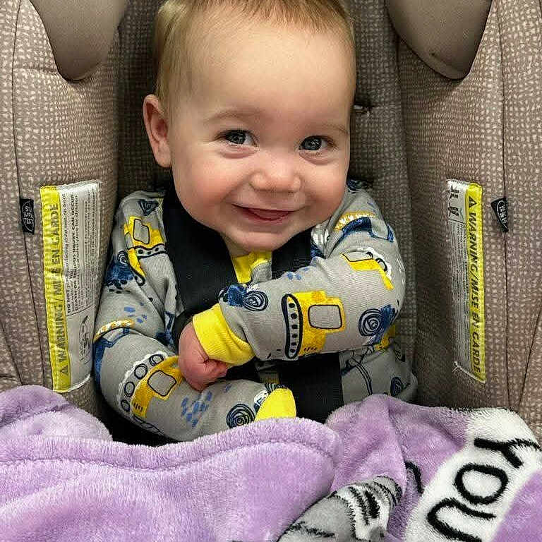 Paxton joined the competition — help win amazing prizes! baby, child, car_seat, blanket, smile, happy, infant, face, clothing, seatbelt, yellow, purple, cute, portrait, sitting, indoors, young, person, safety, cozy
