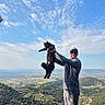 Yoshi participe au concours pour gagner de l'argent avec cette photo : man, cat, outdoor, landscape, hill, nature, sky, cloud, sunlight, sunglasses, cap, smile, holding, animal, pet, casual_clothing, greenery, daytime, scenic, happy