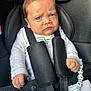 baby, bead_chain, black, blue_eyes, car_seat, child, close_up, cute, fabric, furrowed_brows, hand, indoor, infant, person, portrait, safety_harness, seat_belt, secure, serious_expression, white_clothing