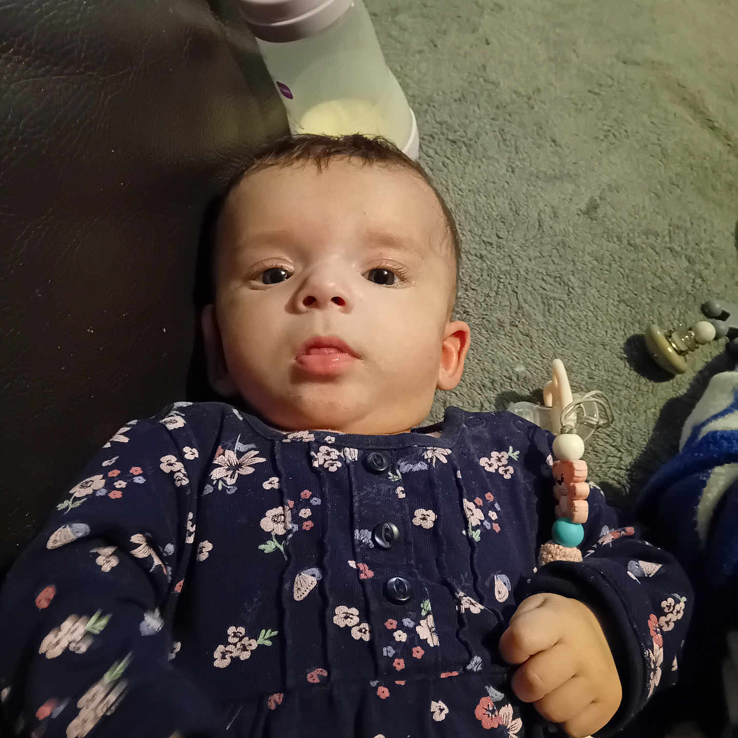 Olga Contulescu participe au concours pour gagner de l'argent avec cette photo : baby, carpet, child, clothing, cute, expression, eyes, face, floor, floral_pattern, hand, indoor, infant, lying_down, milk_bottle, navy_clothing, pacifier_clip, person, toy, young