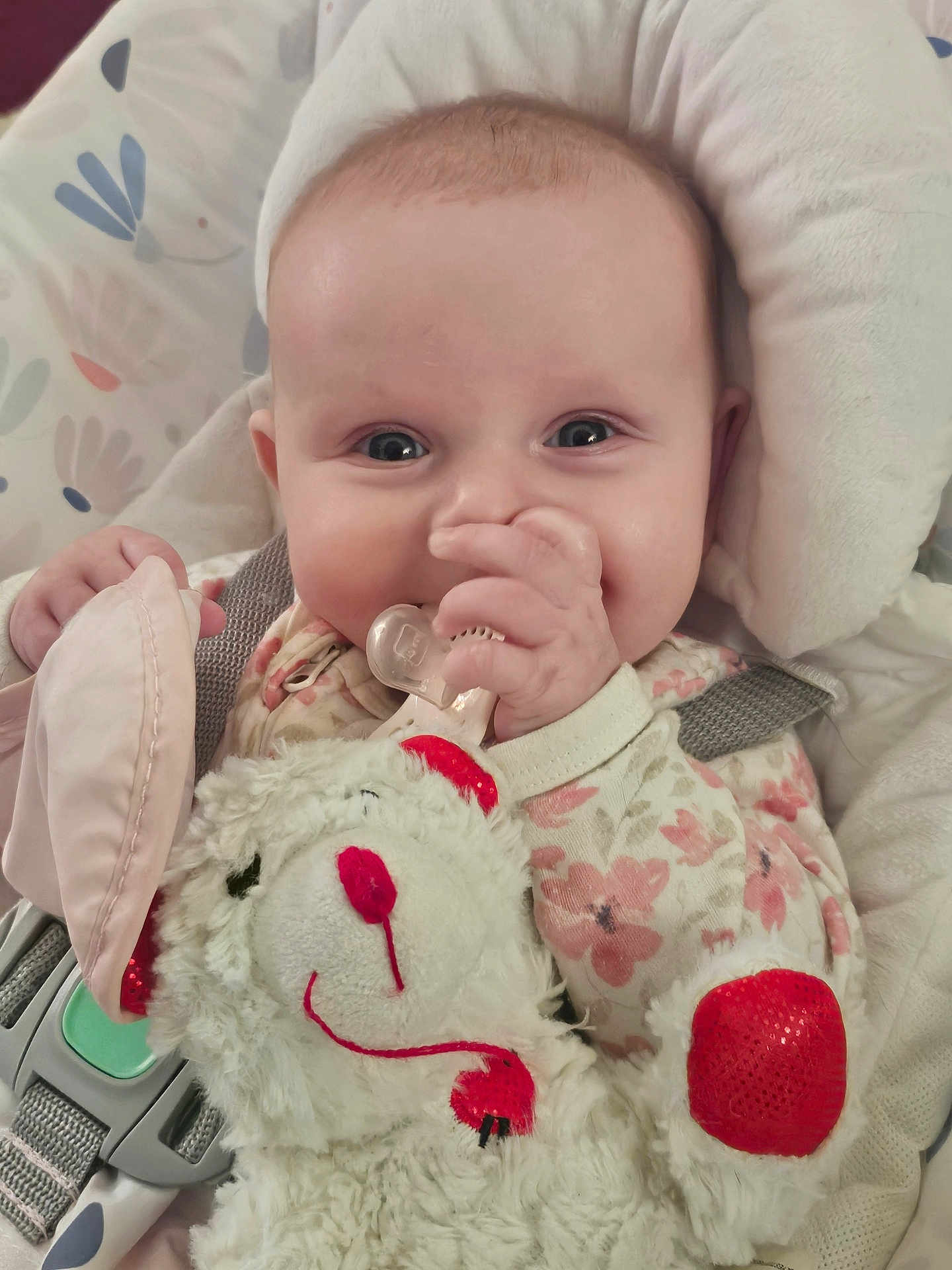 Kara joined the competition — help win amazing prizes! baby, infant, teddy_bear, plush_toy, pacifier, onesie, floral_pattern, cushion, seat_belt, child, cute, smiling, indoors, soft_toy, hand, face, comfort, happy, close_up, portrait
