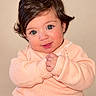 baby, beige_background, blue_eyes, brown_hair, child, clasped_hands, close_up, cute, face, fashion, indoors, infant, knitwear, long_sleeves, peach_sweater, portrait, sitting, smiling, soft_lighting, studio