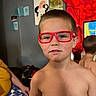 child, boy, red_glasses, shirtless, indoor, portrait, face, short_hair, wall_art, television, living_room, person, home, background, colorful, casual, young, expression, playful, family