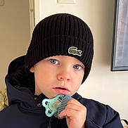 Illan participe au concours pour gagner de l'argent avec cette photo : beanie, blue_eyes, casual, child, closeup, curious, expression, face, hand, hat, headwear, indoor, jacket, pacifier, person, portrait, toddler, warm_clothing, winter_clothing, young_child