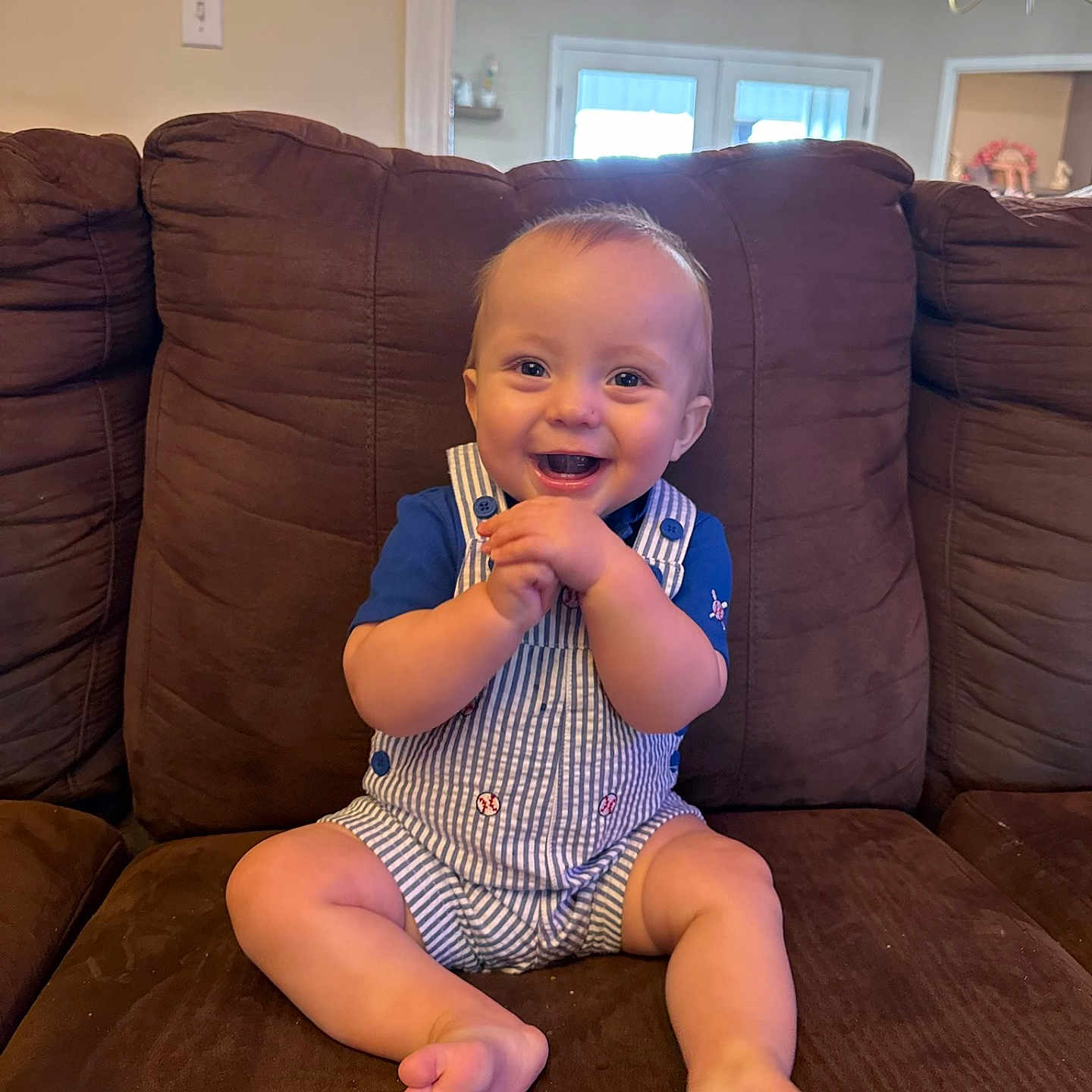 Simon Keith is registered to the contest to win money with this photo: baby, child, smiling, happy, sitting, couch, furniture, indoors, clothing, romper, blue_shirt, hands, face, feet, home, chandelier, window, light, portrait, person