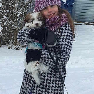 Josie is registered to the contest to win money with this photo: child, girl, dogs, puppies, small_dogs, snow, winter, outdoor, smiling, portrait, hats, winter_clothing, coat, scarf, gloves, purple_pants, leashes, house, snowy_background, pet_carrying
