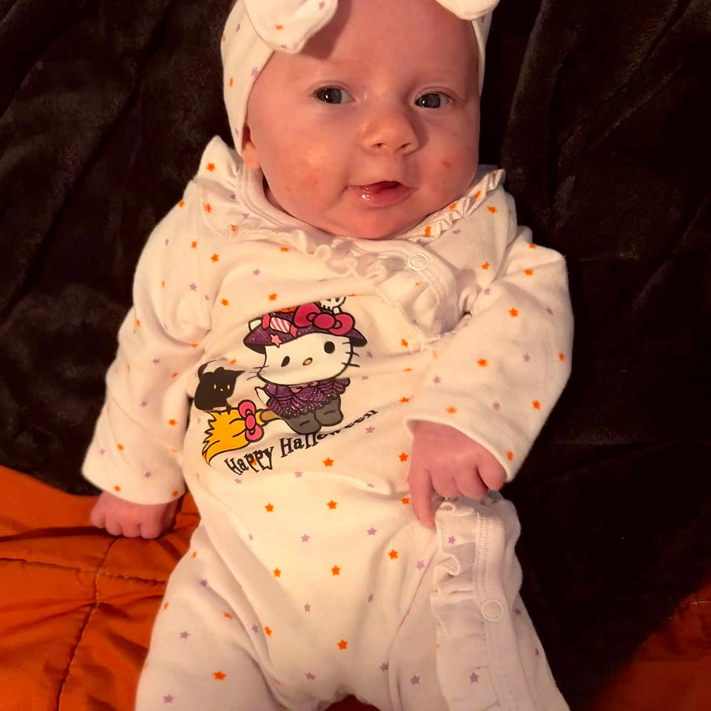 Aerith joined the competition — help win amazing prizes! baby, infant, child, portrait, face, bow, headband, onesie, clothing, hello_kitty, halloween, pumpkin, stars, blanket, indoor, sitting, looking_at_camera, wide_eyes, cute, close_up