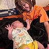 baby, child, siblings, infant, smiling, sitting, lying_down, orange_shirt, yellow_shorts, blanket, couch, indoor, portrait, family, brother, sister, newborn, baby_clothing, cozy, happy