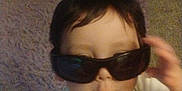 Anthony is registered to the contest to win money with this photo: child, baby, sunglasses, hand, indoor, carpet, furniture, person, cute, face, white_clothing, infant, toddler, portrait, expression, young, holding, glasses, funny, casual