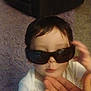 child, baby, sunglasses, hand, indoor, carpet, furniture, person, cute, face, white_clothing, infant, toddler, portrait, expression, young, holding, glasses, funny, casual