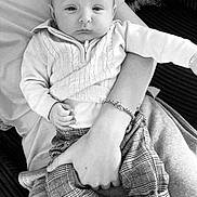 Billy joined the competition — help win amazing prizes! baby, infant, adult, holding, arm, sweater, plaid_pants, shoes, bracelet, black_and_white, calm, indoor, portrait, casual_clothing, person, seated, fabric, hand, closeup, relaxing
