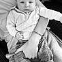baby, infant, adult, holding, arm, sweater, plaid_pants, shoes, bracelet, black_and_white, calm, indoor, portrait, casual_clothing, person, seated, fabric, hand, closeup, relaxing