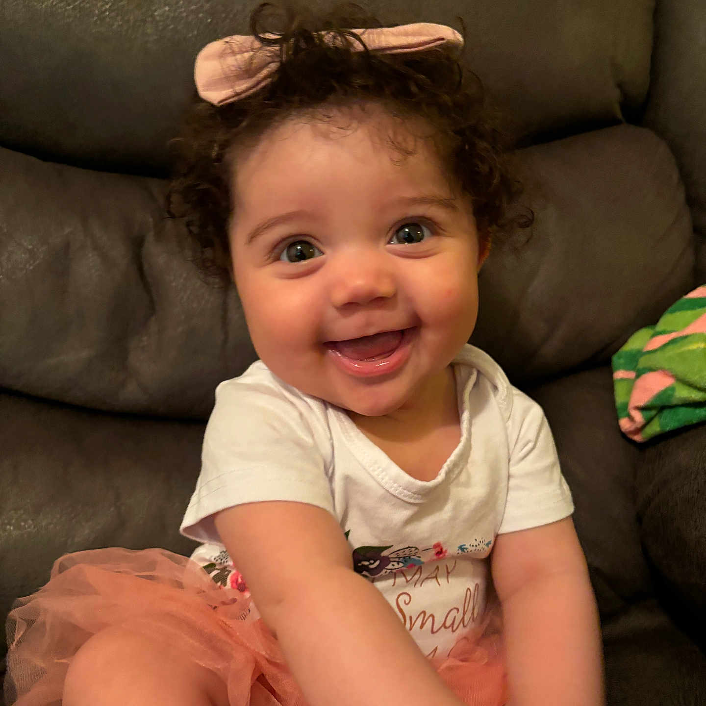 Jemaili is registered to the contest to win money with this photo: baby, child, clothing, couch, cozy, curly_hair, cute, face, happy, headband, indoors, joy, person, pink, portrait, sitting, smiling, toddler, tutu, white_shirt