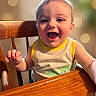 baby, child, high_chair, wood, smile, happy, face, eyes, tank_top, clothing, indoor, person, cute, expression, infant, table, hand, skin, light, bokeh
