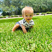 Jaxson is registered to the contest to win money with this photo: baby, child, grass, outdoor, sunny, smiling, crawling, greenery, nature, blue_sky, striped_shirt, shorts, happy, young, person, daylight, portrait, cute, head, eyes